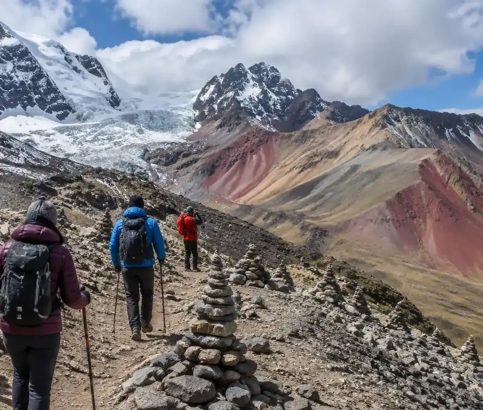 Trekkers crossing a high stony pass on the Ausangate circuit with glaciers and colorful hills