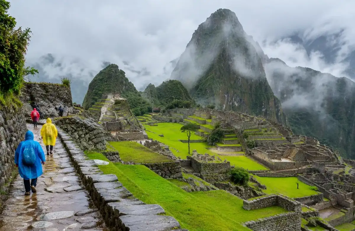 Visitors in rain ponchos at Machu Picchu in December among green terraces and clouds