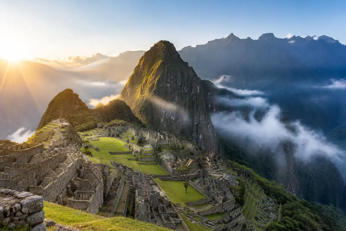 Machu Picchu sunrise light breaking over the peaks beside Huayna Picchu with clouds below