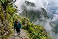 Hiker climbing Inca stone stairs on the Machu Picchu Mountain trail through cloud forest