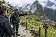 Park guard explaining Machu Picchu rules to visitors beside a one-way route sign