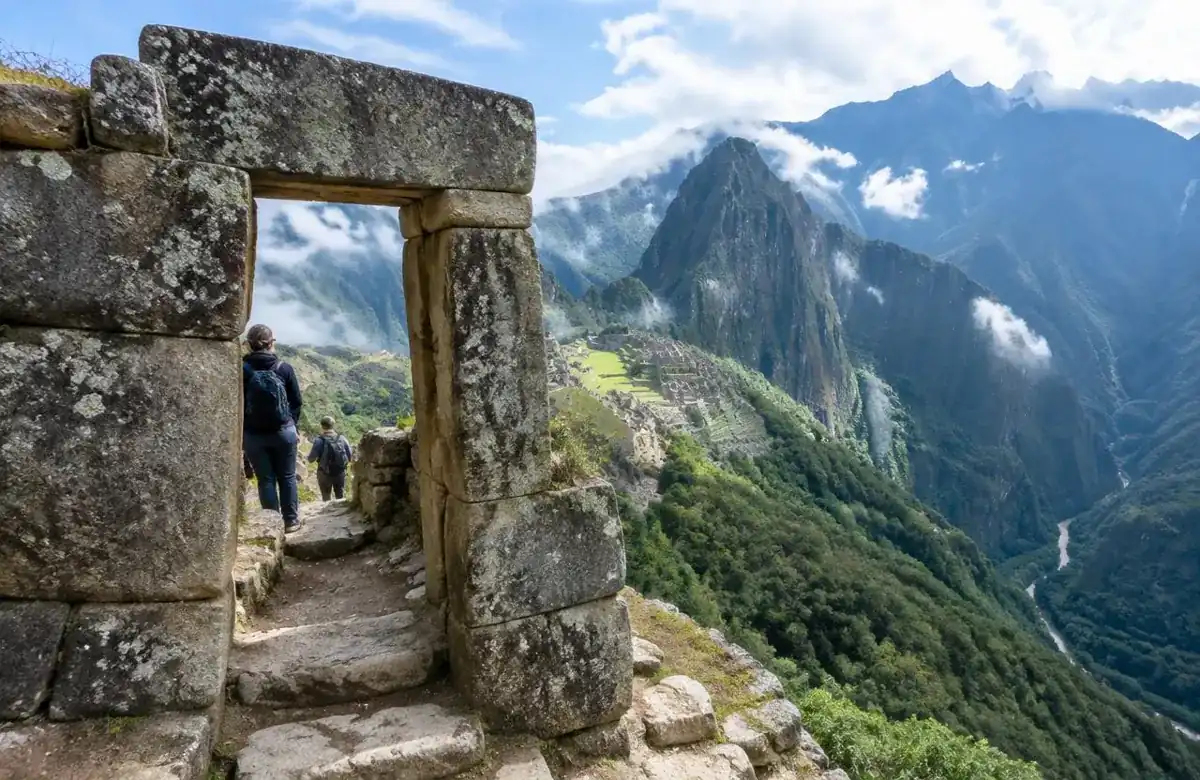 Hikers passing the Inti Punku Sun Gate stone doorway with Machu Picchu citadel far below